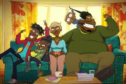 In this still from the 'Good Times' animated series, a Black family of five sits on a teal couch in the living room and poses for a family photo. The mom (short blond hair) smiles nicely in the center of the photo while her adolescent son and daughter playfully jostle one another to her right. Her husband takes up all of the other half of the couch as their baby pulls his hair and cheek.